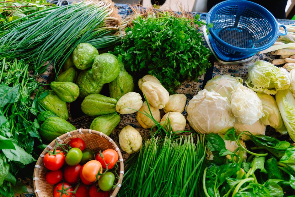 A vibrant display of fresh organic vegetables including tomatoes and chayote on a market table.