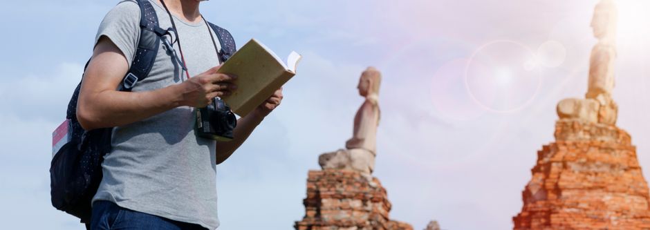 Man with a camera and book exploring ancient ruins under bright sun.