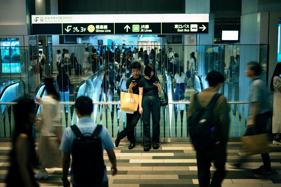 Crowded scene in Shinjuku Station, Tokyo with busy commuters, escalators, and signage.